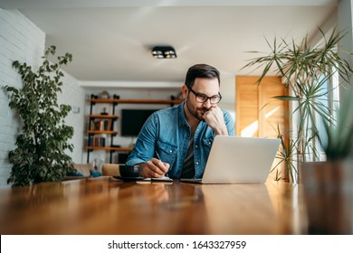 Serious man looking at laptop and taking notes in notebook, portrait. - Shutterstock ID 1643327959