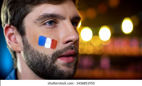 Serious Man With Painted French Flag On Cheek Watching Election Results On Tv