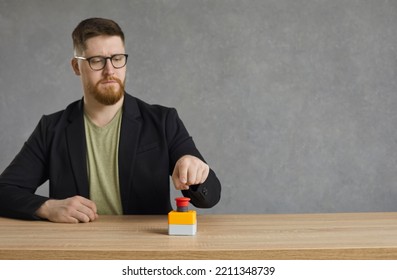 Serious man pushes big red button. Young hipster guy or businessman in glasses hits red alert button on table. Male entrepreneur sitting at desk presses activation button to get access to something - Shutterstock ID 2211348739