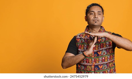 Serious man requesting timeout, doing hand gestures, unable to continue concept. Bold person doing insistent pause sign gesturing, desiring break, isolated over studio background