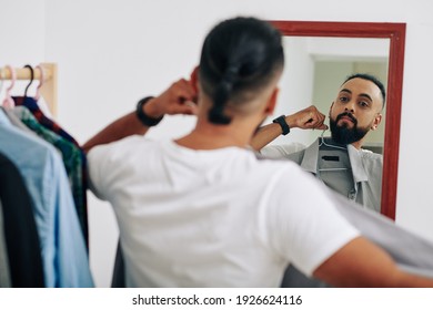 Serious man sanding at mirror and trying on shirt to wear for the first day at work - Powered by Shutterstock