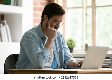 Serious man sit at desk look at laptop screen read e-mail ponder over received information, working remotely, learn new professional business application use modern tech develop online project concept - Shutterstock ID 2182617533
