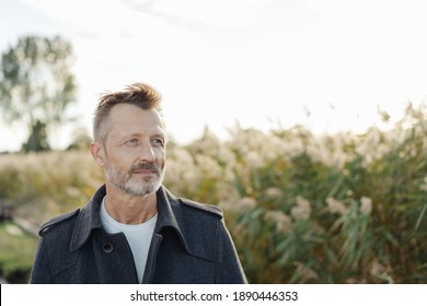 Serious man standing thinking outdoors at the coast alongside tall reeds looking off to the side with a contemplative expression - Powered by Shutterstock