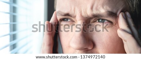Serious man with stress. Ashamed or depressed person. Burnout, amnesia, memory loss or ptsd concept. Migraine or headache. Candid close up of guy rubbing head and touching temples by the window.