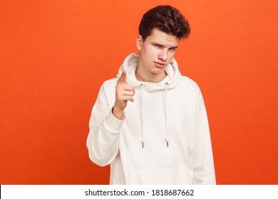 Serious Man In Stylish Hoodie Pointing Finger On You And Watching With Sly Look, Knowing Secret. Blackmail. Indoor Studio Shot Isolated On Orange Background