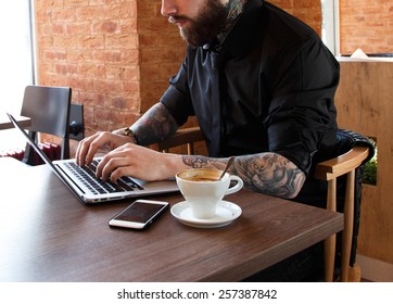 Serious man with tattooes working on a laptop in a coffee shop