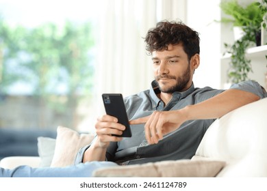 Serious man using smart phone sitting on a couch at home - Powered by Shutterstock