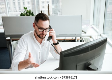 Serious Man In White Shirt Which Sitting By The Table And Talking On Phone