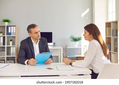 Serious man and woman having business meeting. Employer or HR manager listening to candidate telling about her work experience during job interview. Boss talking to employee sitting at desk in office