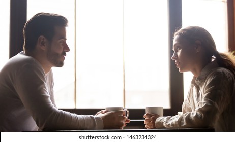 Serious Man And Woman Sitting At Cafe Table Drinking Coffee Talking And Chatting, Millennial Colleagues Or Friends Spend Lunch Break In Coffeehouse Speaking And Sharing News Enjoying Hot Beverage