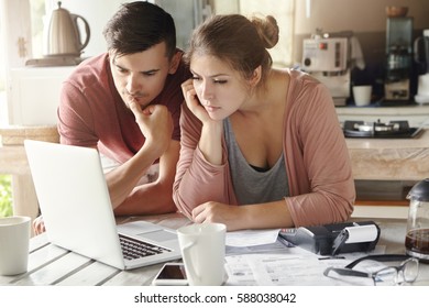 Serious Man And Woman Sitting At Kitchen Table In Front Of Open Laptop Computer, Looking At Screen With Concentrated Expression, Focused On Paying Utility Bills Online. Family Budget And Finances