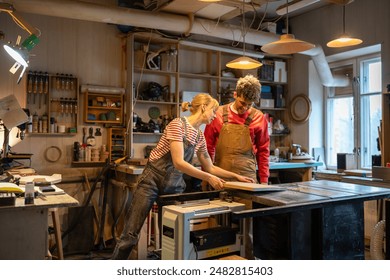 Serious married couple working together in carpentry shop. Attentive spouses engaged in joint small business for manufacture of joinery, making creating wooden products. Man and woman at workshop. - Powered by Shutterstock