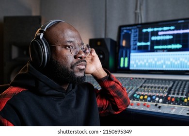 Serious Mature Black Music Producer Wearing Headphones Attentively Listening To Audio Track Thinking About Its Quality