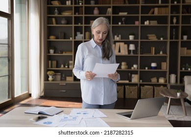 Serious Mature Business Woman Reviewing Project Sales Reports At Home Workplace Table With Laptop, Reading Paper Document, Analyzing Marketing Data, Statistics, Financial Results