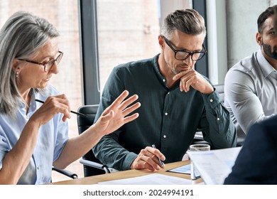 Serious mature caucasian male ceo executive manager with male business partner discussing corporation merge plan at board room table. Professional coworkers leaders doing paperwork in modern office. - Powered by Shutterstock