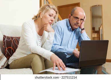 Serious Mature Couple  With Laptop  At Table In Home