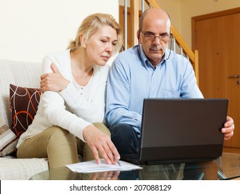  Serious Mature Couple  Looking Documents In Laptop In Home Interior