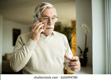 Serious Mature Man Talking On Cell Phone At Home. 