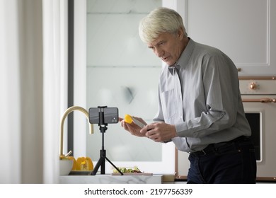 Serious Mature Older Man Filming Cooking Dinner For Blog, Watching Video Recipe Of Salad, Recording Workshop, Showing Slice Of Food At Smartphone Camera, Presenting Organic Ingredients