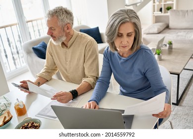 Serious Mature Senior Old Couple Reading Documents Bills Paying Bank Loan Online Together Using Laptop And Phone, Calculating Pension Taxes, Planning Family Retirement Money Finances Working At Home.