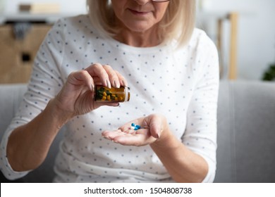 Serious Mature Woman Taking Out Pills From Bottle Close Up, Supplements Or Antibiotic, Older Female Preparing To Take Emergency Medicine, Sitting On Couch At Home, Healthcare And Treatment Concept