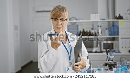 Serious middle age blonde woman scientist ardently sends out voice message from her smartphone whilst working on a medical document in the lab