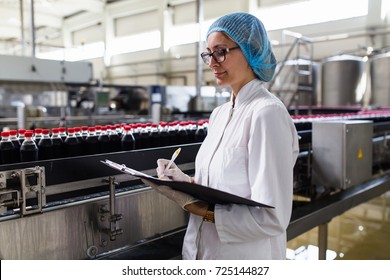 Serious Middle Age Woman Quality Control Worker Checking Robotic Line For Bottling And Packaging Carbonated Black Juice Of Soft Drink Into Bottles.