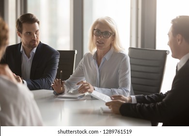 Serious Middle Aged Businesswoman Talks At Group Board Executive Meeting, Confident Mature Old Female Leader Speaking Discussing Work Offers Solution Negotiating With Partners At Corporate Briefing