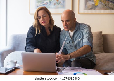 Serious Middle Aged Couple Consulting Internet About Interior Design. Caucasian Man And Woman In Casual Holding Swatches And Drawings, Using Computer. Renovation Concept