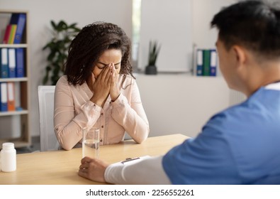 Serious middle aged korean doctor calms crying black millennial female patient, giving glass of water in clinic office interior. Health problem, visit to therapist, reaction bad news about disease - Powered by Shutterstock