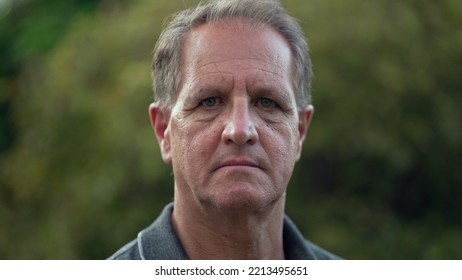 Serious Middle Aged Man Standing At Park Looking At Camera. Portrait Of An Older Male Person With Arms Crossed