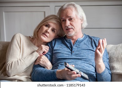 Serious Middle Aged Senior Couple Embracing Talking Watching Tv Together At Home, Retired Mature Older Family Talking Discussing Television News With Remote Control Sitting On Sofa In Living Room