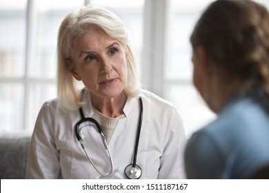 Serious Middle-aged Female Doctor Pediatrician Talk With Little Girl Patient Show Support And Care, Attentive Senior Woman Psychologist Or Nurse Speak Give Help Do Checkup Of Child At Home