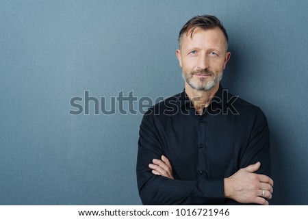 Serious middle-aged man with folded arms and a deadpan expression posing in front of a grey background with copy space