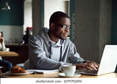 Serious millennial african-american man using laptop sitting at cafe table, focused black casual guy communicating online, writing emails, distantly working or studying on computer in public place