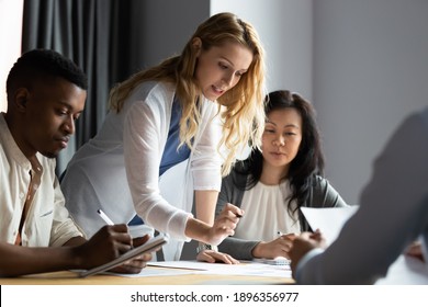 Serious millennial blonde female team leader analyzing financial or marketing paper document, reporting research results to focused multiracial young and older business partners colleagues at office. - Powered by Shutterstock