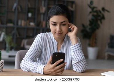 Serious Millennial Mixed Race Woman Sit At Desk Read Text On Smartphone Screen Use Mail Client To Send Receive Message Browse Web. Concentrated Teen Female Hold Cell Chat In Convenient App Check Email