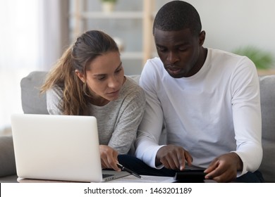 Serious mixed race young couple calculating paying domestic bills with laptop at home, interracial family planning expenses using calculator managing budget money insurance finance taxes do paperwork - Powered by Shutterstock