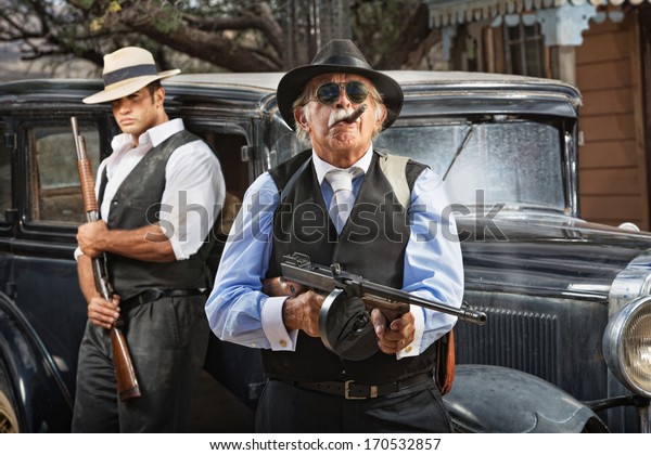 Serious mob boss\
with gun and guard near\
car