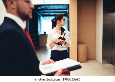 Serious multiethnic coworkers in formal suits standing in modern office corridor and talking about business strategy together while waiting for elevator - Powered by Shutterstock