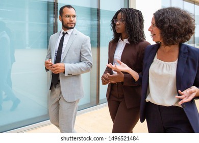 Serious Multiethnic Coworkers Walking And Talking. Male And Female Business Colleagues In Formal Wear Talking While Walking Outside Office Building. Cooperation Concept