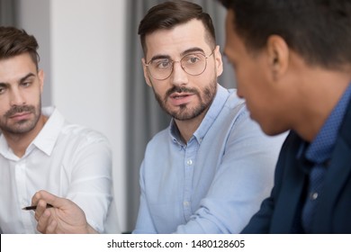 Serious Multi-ethnic Work Team Sit At Desk Talk Brainstorming On Project Strategy, Focus On Confident European Team Leader, Diverse Employees Discuss Share Ideas Cooperating Together At Office Meeting