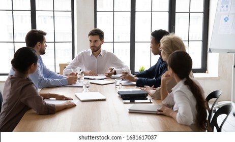 Serious Multiracial Businesspeople Gather At Desk In Office Discuss Business Ideas Together, Focused Male Team Leader Hold Meeting With Diverse Coworkers In Boardroom, Cooperation Concept