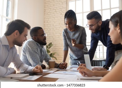 Serious multiracial corporate business team and black leader talk during group briefing, focused diverse colleagues brainstorm discuss report paperwork engaged in teamwork at meeting gather at table - Shutterstock ID 1477336823