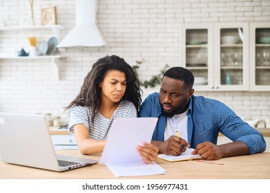 Serious multiracial young couple study documents together, have serious looks, dressed in casual wear, plan their budget, pose in spacious light room, do paperwork, busy preparing financial report - Powered by Shutterstock