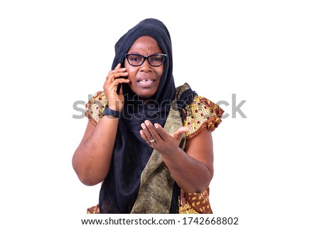 serious muslim mature woman with glasses talking on cellphone while gesturing hand.