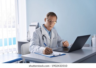 Serious Old Mature Professional Male Doctor Using Laptop Computer In Hospital Office Watching Medical Webinar Training, Writing In Healthcare Report, Consulting Patient Online At Telemedicine Meeting.