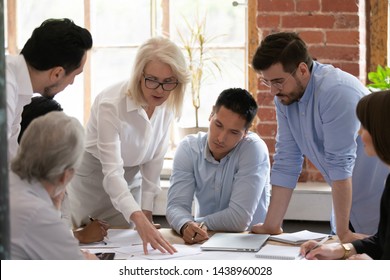 Serious old mature woman team leader coach teach young workers explain paper business plan at group meeting, focused senior female teacher mentor training diverse staff at corporate office workshop - Shutterstock ID 1438960028