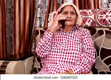 Serious Old Women Of Indian Ethnicity Sitting On Sofa At Home And Talking On Mobile Phone.   