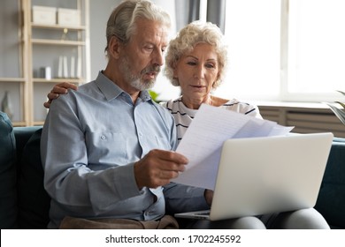 Serious Older Couple Managing Planning Budget Together, Reading Loan Or Mortgage Documents, Mature Woman And Man Checking Bills, Domestic Finances, Using Laptop, Sitting On Couch In Living Room